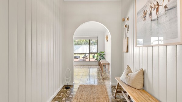 A hallway with a tiled floor, a bench, and a view of an outdoor area with a patio and plants. - Coastline Callala - Fire Pit - Pet Friendly (Callala Beach)