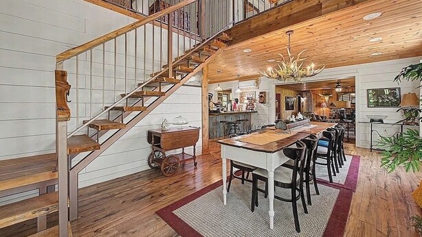 Un interior espacioso con una escalera de madera, un comedor con una mesa larga y una cocina al fondo.