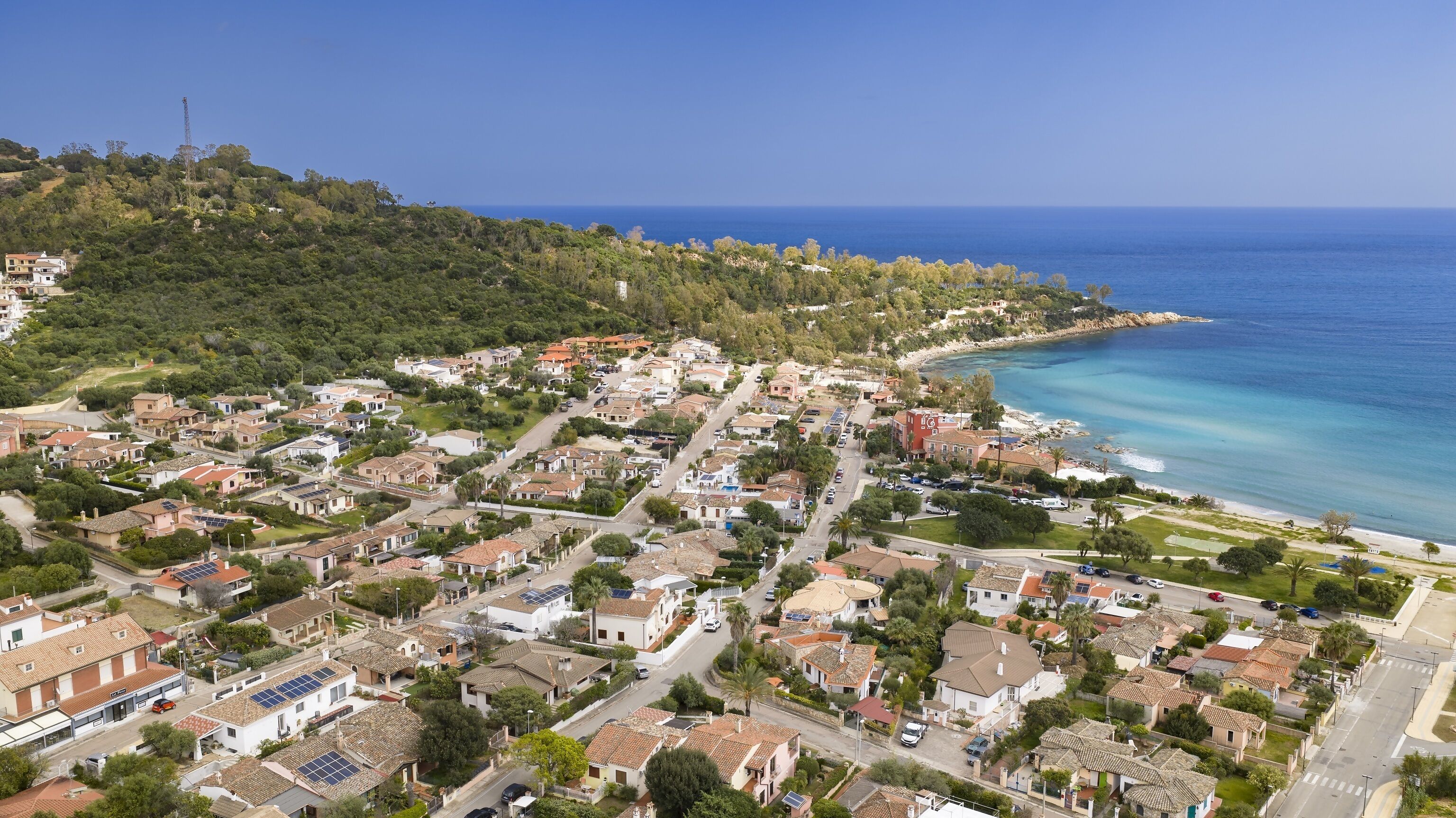 An aerial view of a coastal town with residential buildings, a beach, and a clear blue sky.