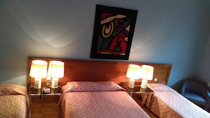 Una habitación de hotel con dos camas, lámparas de noche, un teléfono y un cuadro en la pared.