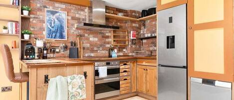 A kitchen with brick walls, wooden cabinets, a stainless steel refrigerator, and a built-in oven.