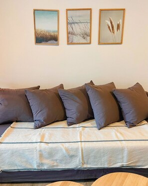 Un canapé doté de plusieurs coussins et, au-dessus, trois tableaux encadrés accrochés au mur.