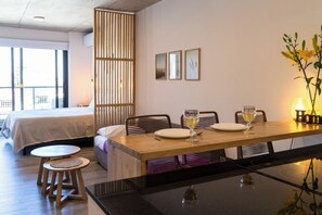 Una habitación de hotel moderna con zona de comedor, cama y vistas al exterior.