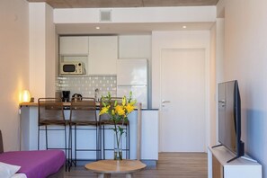 Un espacio habitable compacto con kitchenette, zona de comedor con dos sillas, una mesa redonda pequeña, sofá y televisor.
