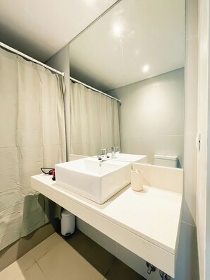 Ein modernes Badezimmer mit einem weißen Waschbecken, einem Spiegel und einer Duschvorhang.