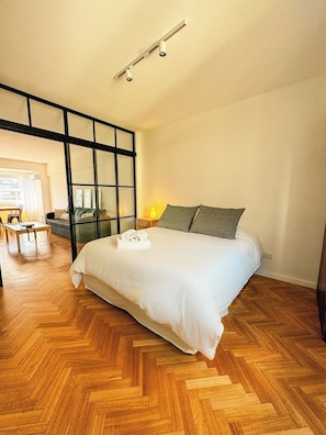 A bedroom with a wooden herringbone floor, a bed with white bedding, a desk, and a chair. - Brand new and comfortable in a central location by BT Homes (ABJ)