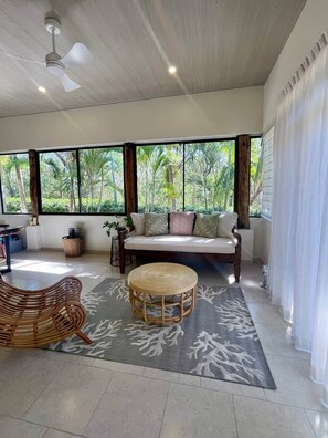 A room with a large window, a sofa, a round wicker table, and a ceiling fan. - Villa Të Sula • House of Peace • Coastal Nature Escape (Cabo Velas)