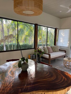A room with a large window, a wooden dining table, a sofa, and a hanging light fixture. - Villa Të Sula • House of Peace • Coastal Nature Escape (Cabo Velas)