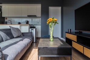 Ein modernes Wohnzimmer mit einer Couch, einem Couchtisch, einem Fernseher und einer Küche im Hintergrund.