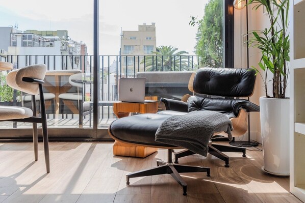 Un balcón moderno con un sillón de cuero, una computadora portátil y una planta en maceta.
