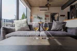 Un salón moderno con un sofá gris, dos copas de vino y vistas amplias a través de grandes ventanales.