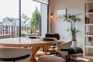 Un comedor moderno con una mesa redonda, sillas y dos copas de vino. Se ve una estantería con libros y objetos decorativos al fondo.
