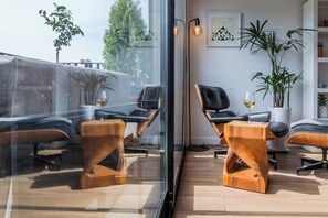 Ein modernes Wohnzimmer mit Glaswand, zwei Ledersesseln, einem Holztisch und einem Blumentopf.