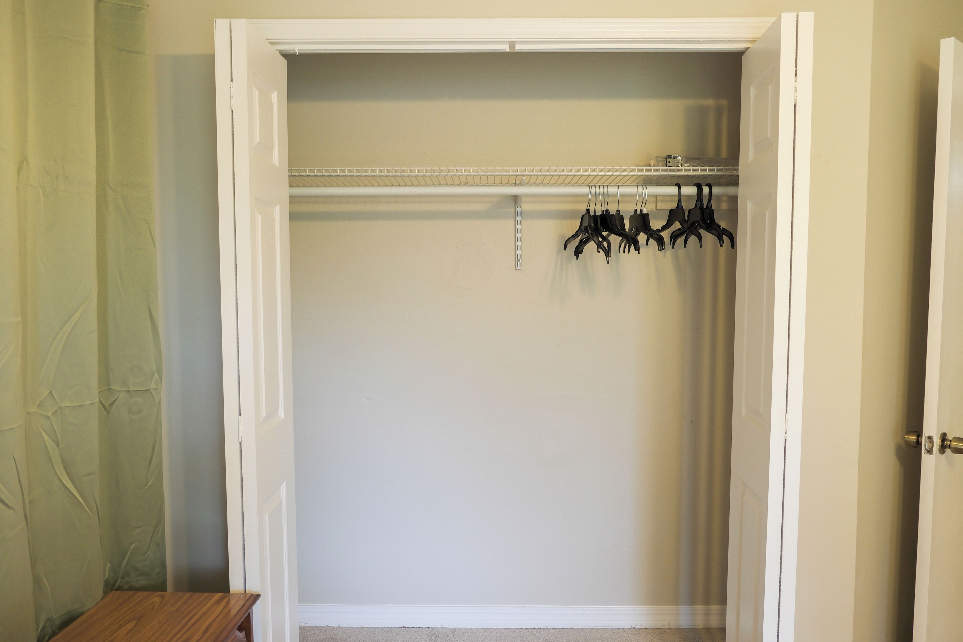 Ein begehbarer Kleiderschrank mit weißer Tür, einer Holzbank und einem Kleiderständer mit Kleiderbügeln.