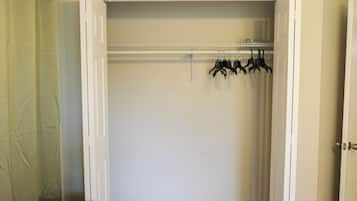 Ein begehbarer Kleiderschrank mit weißer Tür, einer Holzbank und einem Kleiderständer mit Kleiderbügeln.