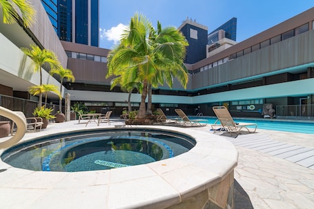 A swimming pool with lounge chairs, palm trees, and modern buildings in the background.. Cozy 1-bedroom apartment with Sofa bed and AC in peaceful Honolulu