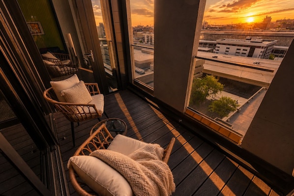 A balcony with wicker chairs and a view of the cityscape at sunset.
