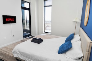 A modern hotel room with a bed, a TV mounted on the wall, a window, and a lamp.