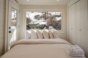 Ein Schlafzimmer mit einem Bett, Kissen, einem Fenster und Blick auf eine verschneite Landschaft.