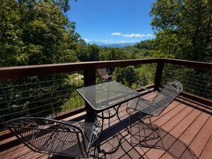 A deck with a table and chairs, overlooking a forested landscape. - Blu's Blessed View-1BR cabin that sleeps 4, Hot Tub, Mountain VIEW & arcade fun (Sevierville)