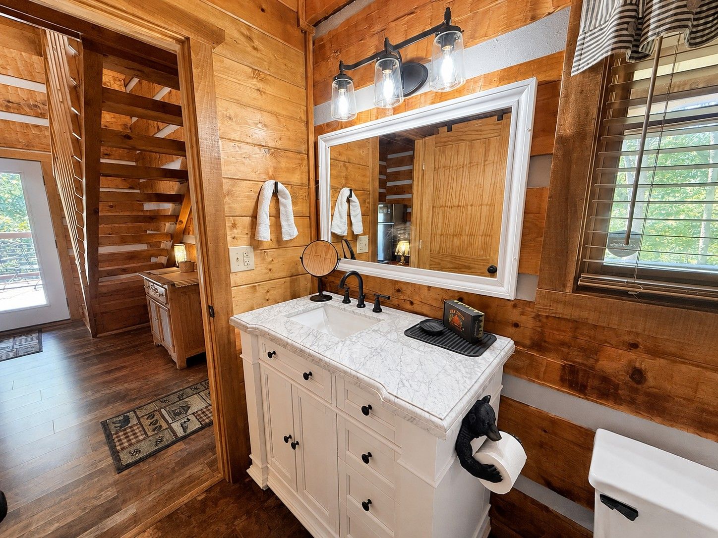 A wooden cabin bathroom with a white vanity, a mirror, and a window with blinds.