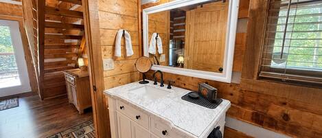 A wooden cabin bathroom with a white vanity, a mirror, and a window with blinds.