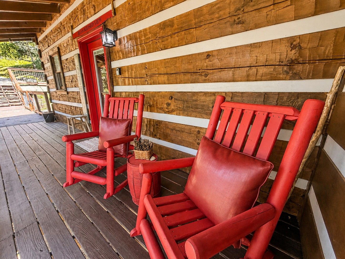 Twee rode stoelen op een houten terras, met een houten wand en een deur waarop 'BEHOLD VIEW' staat.