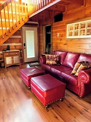 Ein Holzinnenraum mit einem roten Ledersofa, einem Hocker und einer Treppe.
