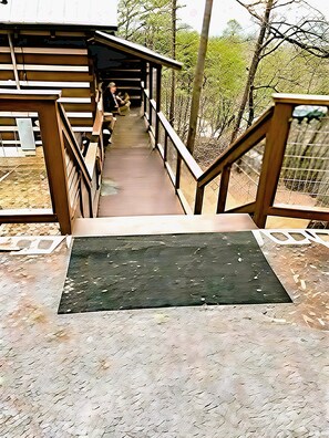Eine Holzbrücke mit Metallgeländern, die zu einem überdachten Bereich mit Bänken führt.