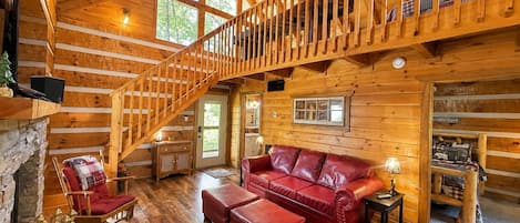 A log cabin interior with a wooden staircase, a red leather sofa, and a stone fireplace.