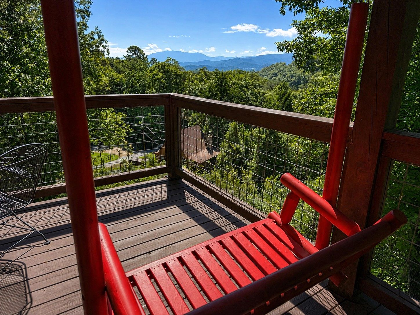 A wooden deck with a red bench, metal railing, and a view of a mountainous landscape.