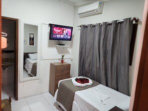 Habitación de hotel con cama, televisión, armario, espejo y zona de ducha.