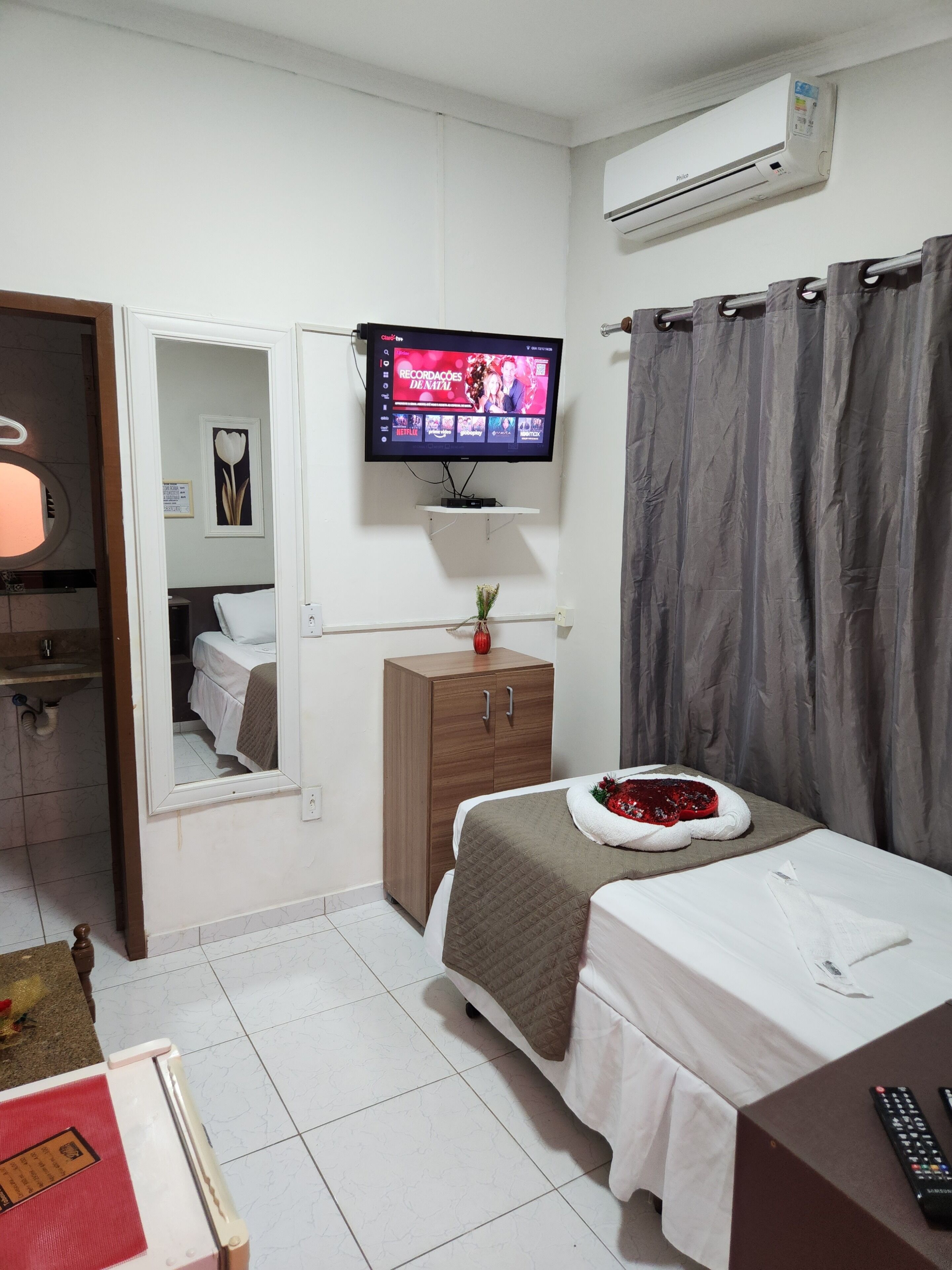 A hotel room with a bed, a TV mounted on the wall, a wooden cabinet, and a bathroom visible through an open door.