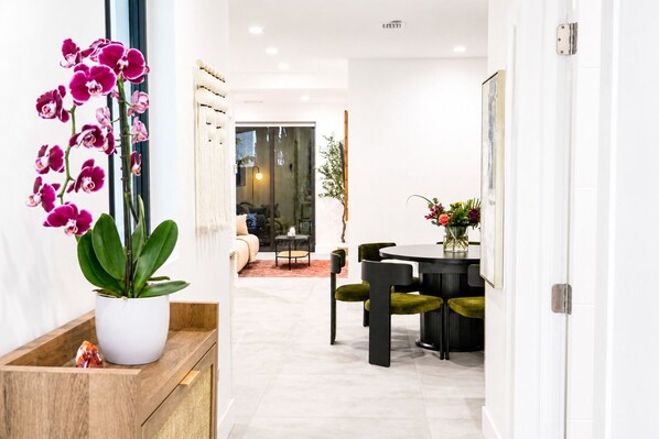 A modern interior with a potted orchid, a dining area with green chairs, and a view into another room. - Luxury New 4BR/4BA Executive Home-Sleeps 8  Workspace-Backyard-Parking (Miami)