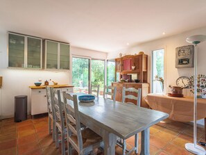 Een keuken met een eettafel, stoelen, een prullenbak en een raam.
