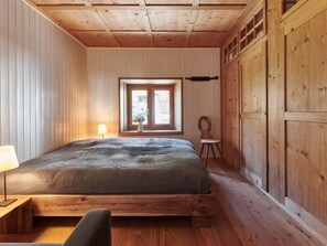 Une pièce aux murs lambrissés, contenant un lit, une fenêtre, une lampe et une chaise.