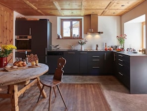 Eine moderne Küche mit dunklen Schränken, einem Holztisch und einer rustikalen Decke.