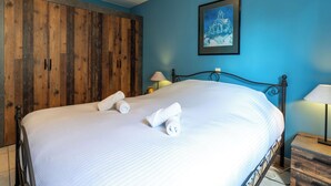 A neatly made bed with white linens and rolled towels, a wooden wardrobe, a framed picture on the wall, and a bedside table with a lamp. - Breduynia 0401 with parking by Interhome (Bredene)