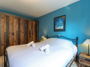 A neatly made bed with white linens and rolled towels, a wooden wardrobe, a framed picture on the wall, and a bedside table with a lamp. - Breduynia 0401 with parking by Interhome (Bredene)