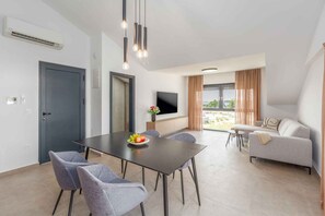 Ein modernes Wohnzimmer mit Essbereich, einer Couch, einem Fernseher und einem großen Fenster mit Vorhängen.