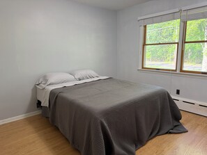 Ein Schlafzimmer mit Bett, Fenster und Blick auf Grünfläche.