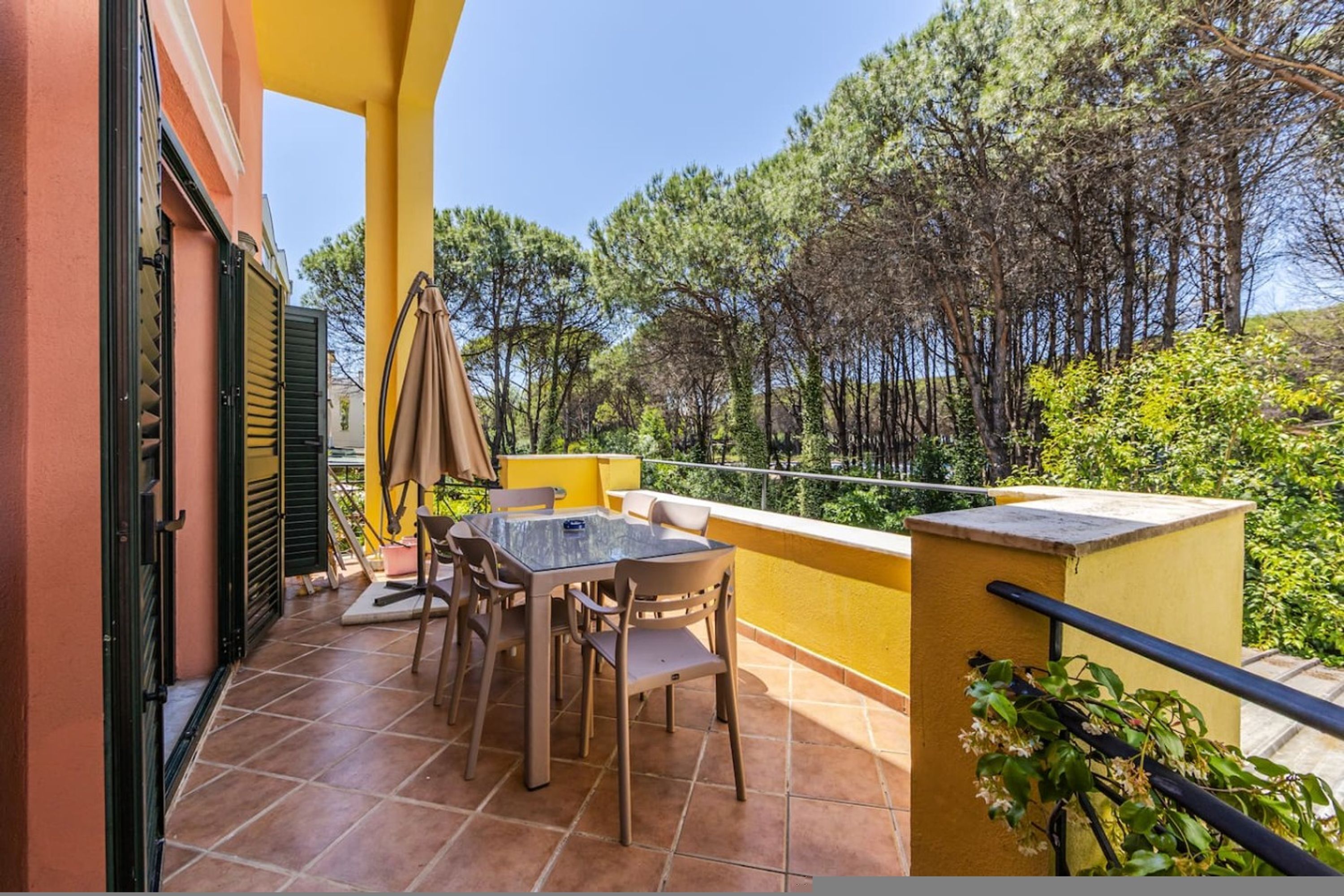 A balcony with a table and chairs, a potted plant, and a view of trees.