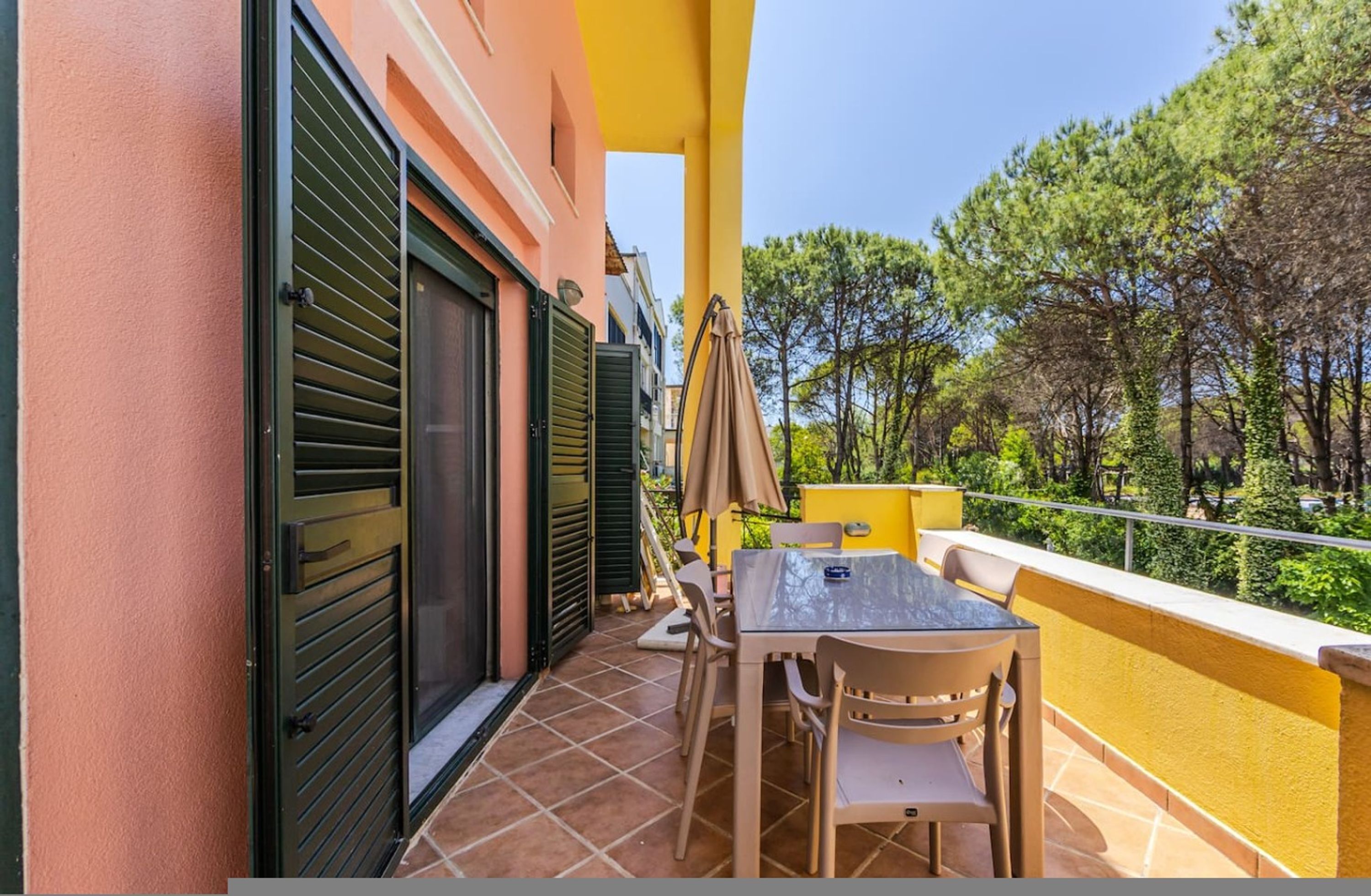 A balcony with a table and chairs, a closed shutter door, and a view of trees.