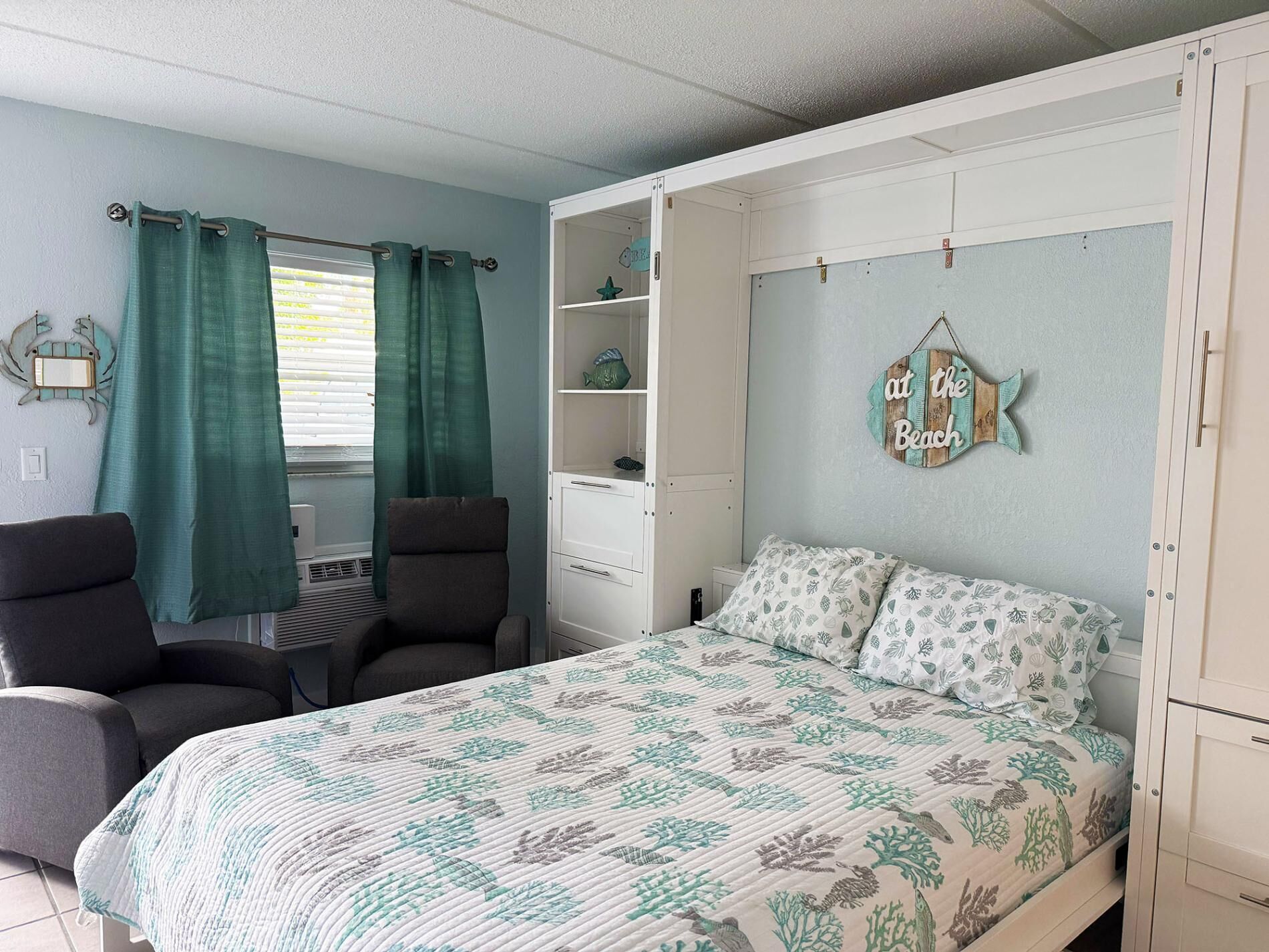 Une chambre à coucher comprenant un lit, deux chaises, une petite table, une commode et un élément décoratif mural.