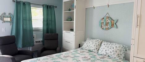 Une chambre à coucher comprenant un lit, deux chaises, une petite table, une commode et un élément décoratif mural.