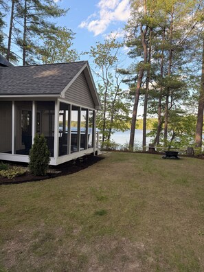 A house with a covered porch, a small lawn, and a view of a lake.