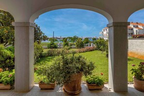 Ein überdachter Außenbereich mit Blick auf einen gepflegten Rasen und Gebäude im Hintergrund.