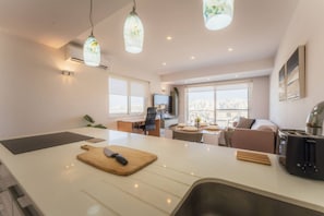 A modern kitchen with a central island, a dining area with a table and chairs, and a living space with a sofa and a TV. - Modern Apt in Marsaskala Near Seafront Beaches (Marsaskala)