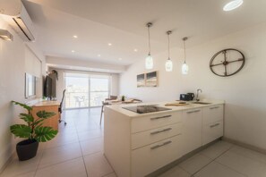 A modern kitchen with a central island, pendant lights, a wall clock, and a large window. - Modern Apt in Marsaskala Near Seafront Beaches (Marsaskala)
