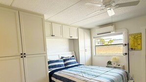 Une chambre à coucher avec un lit, des armoires blanches, un ventilateur de plafond, un appareil de climatisation, une fenêtre donnant sur un beau paysage et une carte accrochée au mur.
